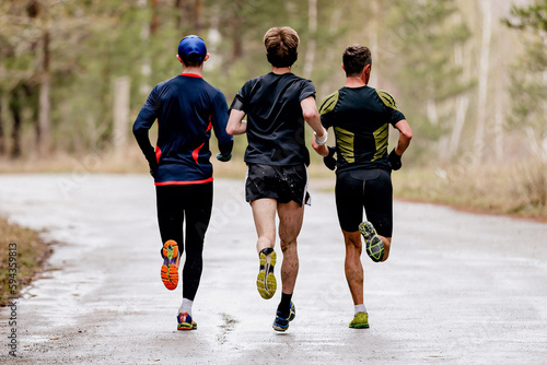 rear view three male runners running spring running on road in with puddles, splashes water and dirt on feet