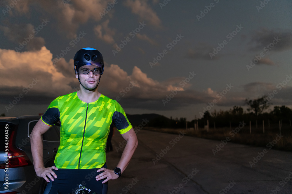 A triathlete resting on the road after a tough bike ride in the dark night, leaning on his bike in complete exhaustion 