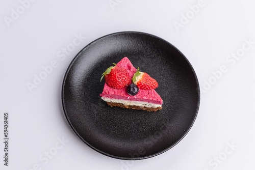 Delicious slice of strawberry-topped cheesecake on a matte dark grey plate on a white background