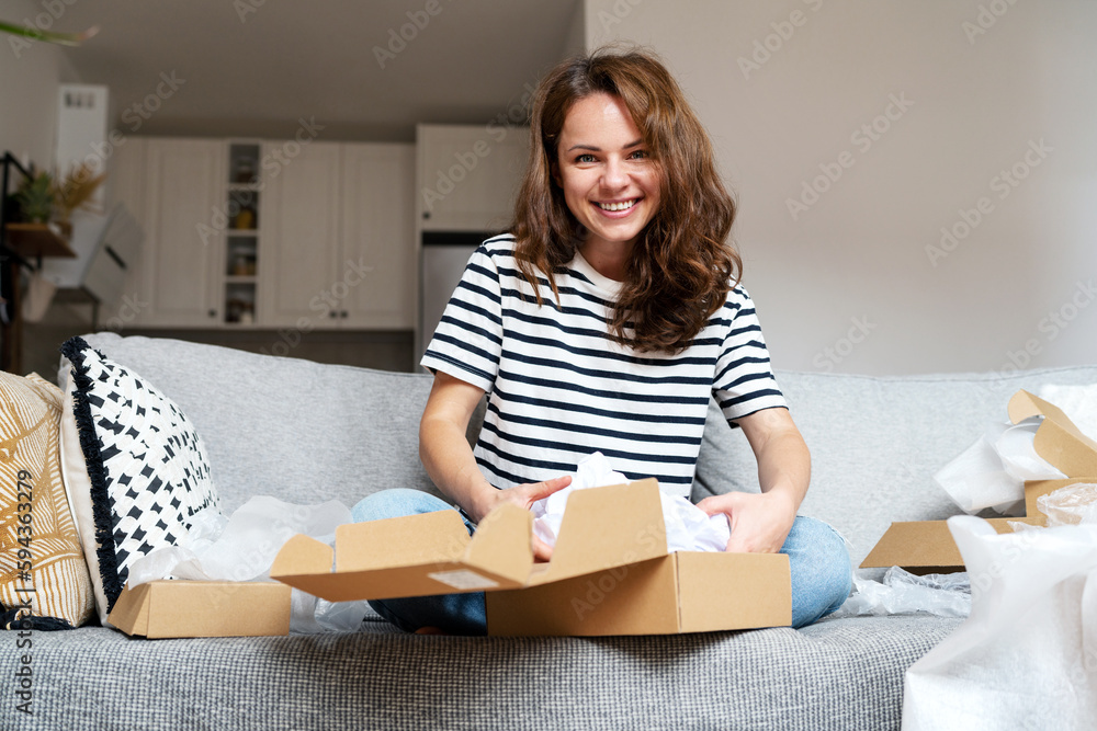 Curly woman unpacking a package, opening a cardboard box with online purchases. Curly woman unpacking a package, opening a cardboard box with online purchases.