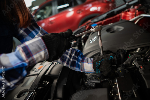 Female auto mechanic unscrewing a nut to replace a car spark plug. © Михаил Решетников