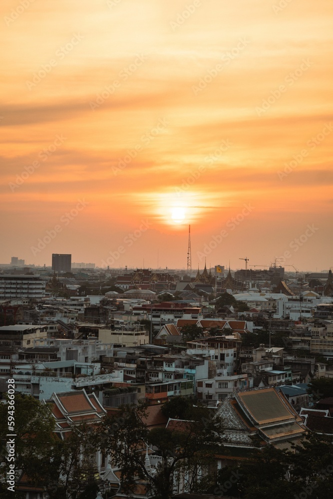 Skyline of Bangkok at sunset, with the bright sun glowing in the orange sky. Thailand.