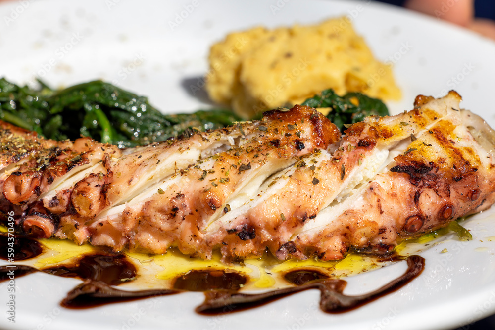 Traditional greek cuisine, grilled octopus sprinkled with herbs, with additions, dish on a plate in a restaurant, Greece