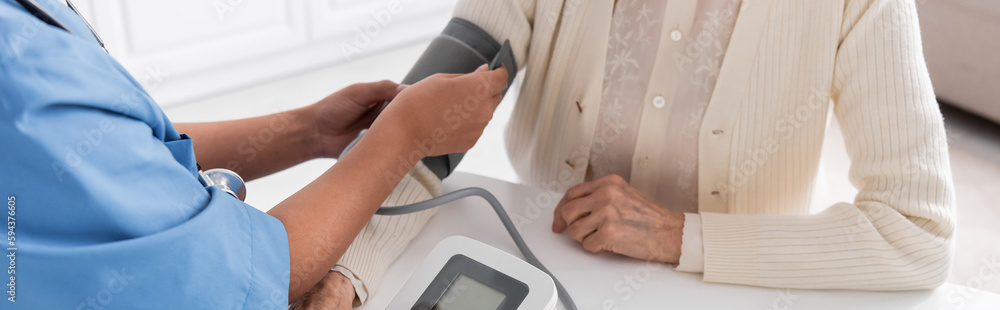 cropped view of multiracial nurse measuring blood pressure of senior woman, banner.
