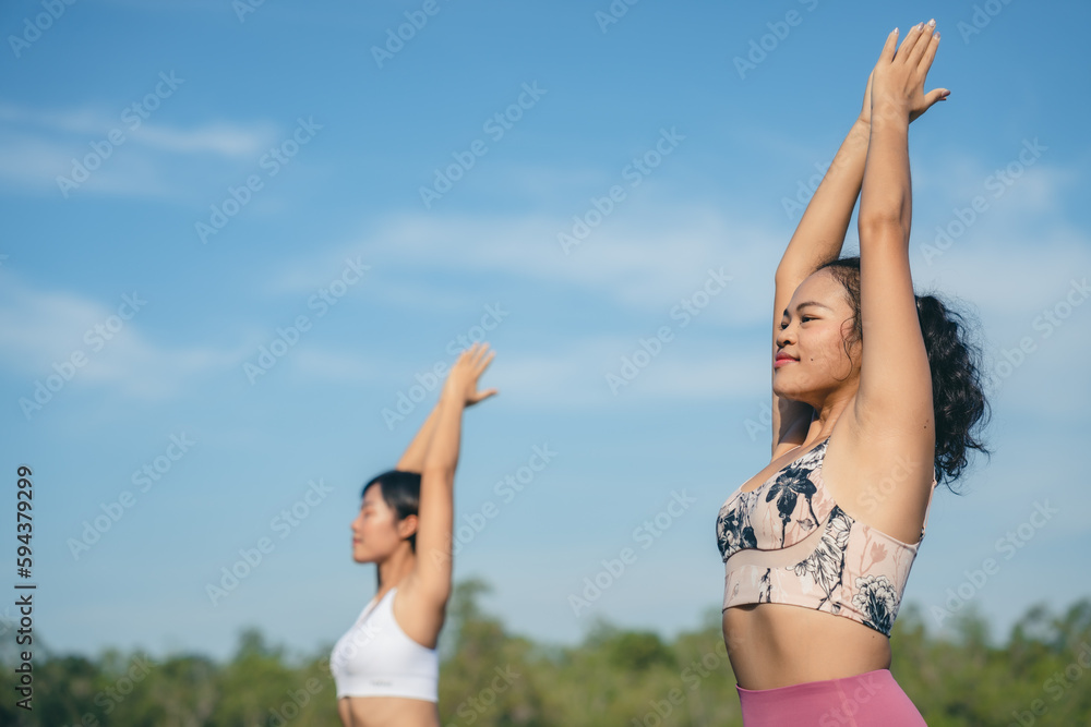 Group of people doing yoga exercises by the lake at morning outdoor, Woman practicing yoga in lotus position at park, Multinational women doing breathing exercises or yoga meditation during outdoor Group of people doing yoga exercises by the lake at morning outdoor, Woman practicing yoga in lotus position at park, Multinational women doing breathing exercises or yoga meditation during outdoor