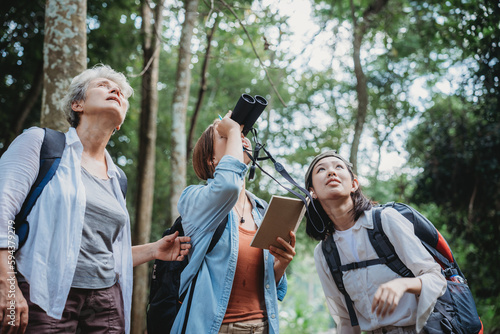 woman family walking in the forest to watching a bird in nature, using binocular for birding by looking on a tree, adventure travel activity in outdoor trekking lifestyle, searching wildlife in jungle