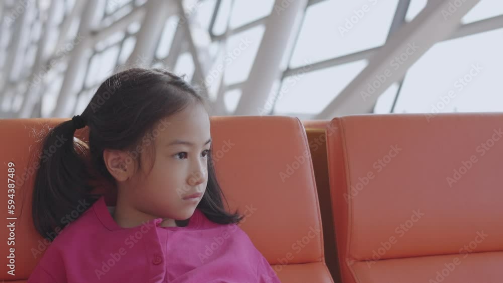 Close up face of adorable asian kid girl who is sitting on bench at airport terminal alone shows concept of waiting, lost, unhappy or depressed emotion of child with beautiful sunlight through window. Close up face of adorable asian kid girl who is sitting on bench at airport terminal alone shows concept of waiting, lost, unhappy or depressed emotion of child with beautiful sunlight through window.