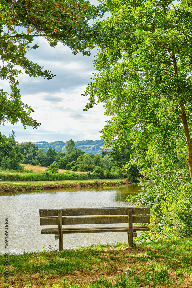 A bench overlooking a lake in the countryside, surrounded by farmland and a forest close to Lyon, France. A quiet place to relax and reflect. Find some peace and tranquility outside in nature