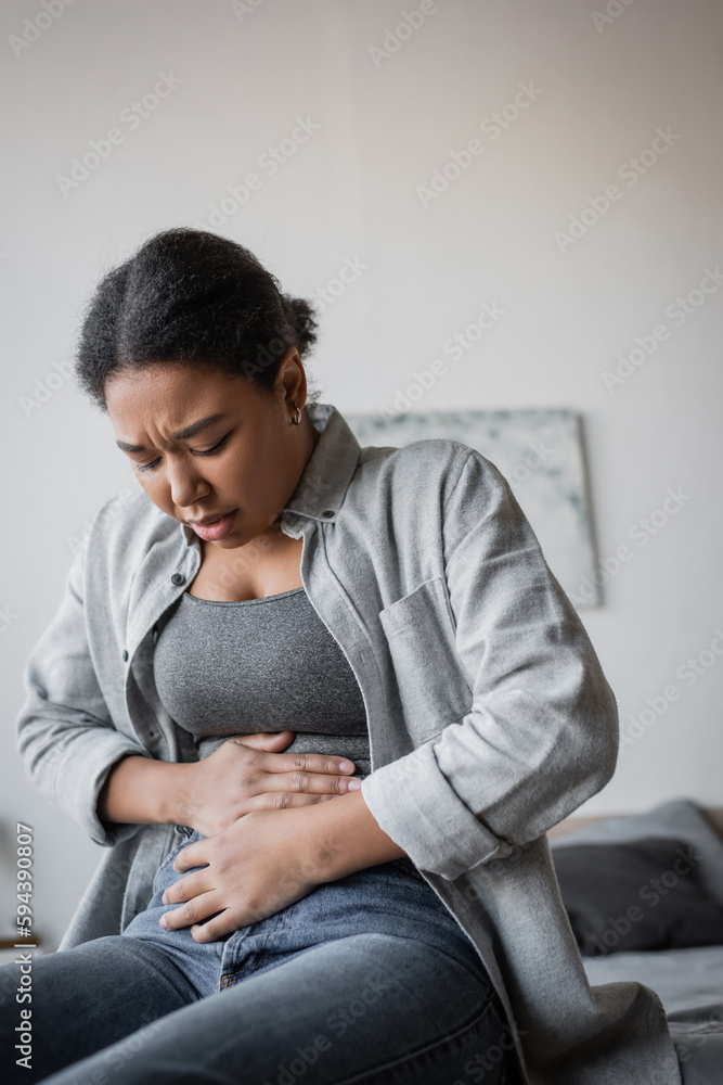 Upset multiracial woman having abdomen pain on bed at home. Upset multiracial woman having abdomen pain on bed at home.