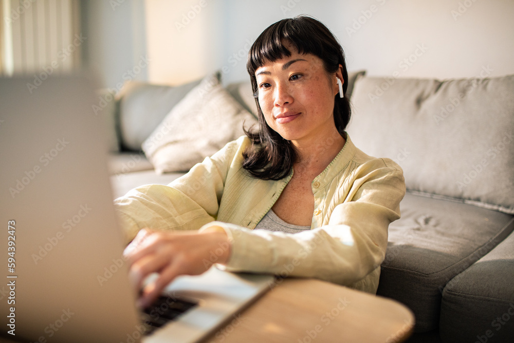 Fototapeta premium Young Japanese Woman using a laptop on a couch