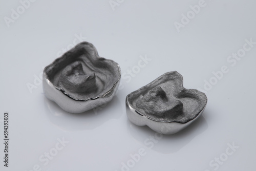 Laboratory pieces of dental metal endo-crown placed upside down on reflective white acrylic plate