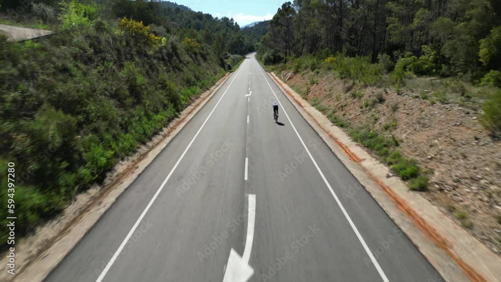 Fit man on triathlon bicycle is training on empty mountain road.Cyclist riding on time trial bike.Athlete is wearing sportswear and aero helmet.Cyclist is preparing for the triathlon competition.Spain Fit man on triathlon bicycle is training on empty mountain road.Cyclist riding on time trial bike.Athlete is wearing sportswear and aero helmet.Cyclist is preparing for the triathlon competition.Spain