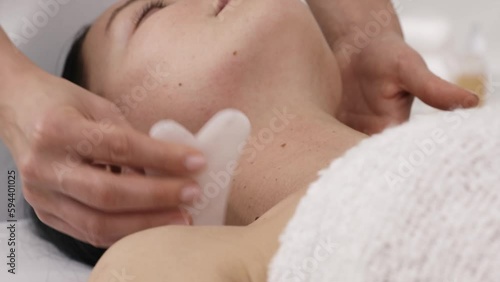 Woman receiving facial massage with guasha tool in beauty salon. 