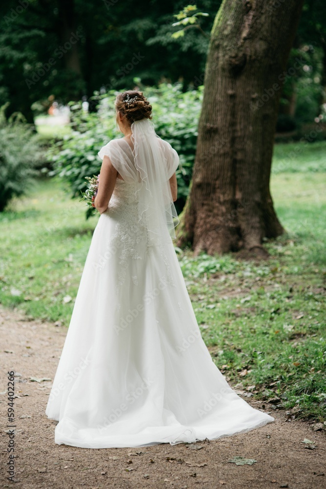 Female dressed in a white bridal dress in a green park