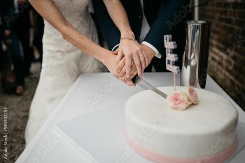 Groom and bride cutting a freshly-baked white cake with a silver knife