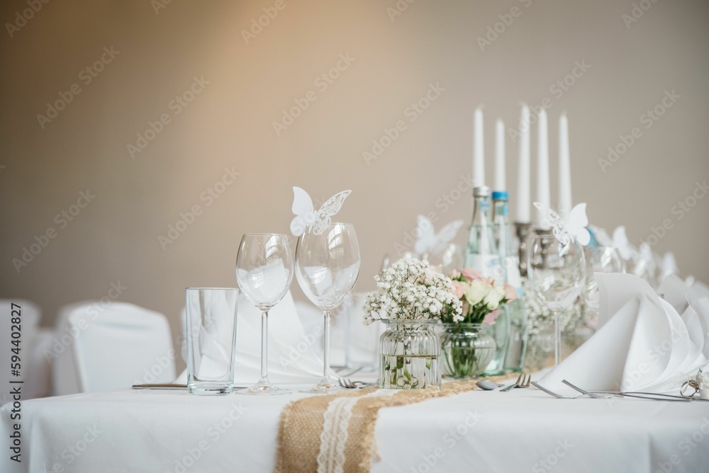 Tastefully decorated table featuring a set of wine glasses and a bouquet of white flowers Tastefully decorated table featuring a set of wine glasses and a bouquet of white flowers