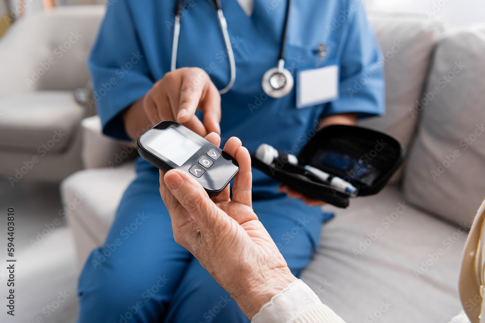 partial view of multiracial nurse pointing at glucometer in hand of senior woman.