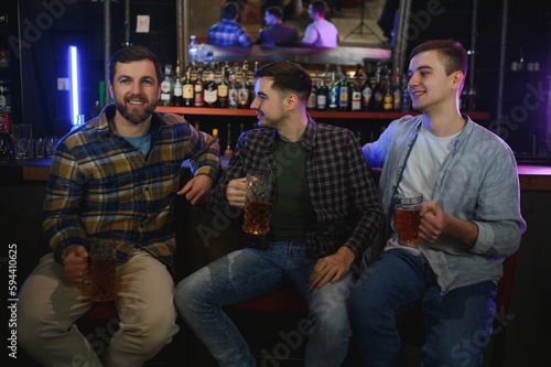 Young men in casual clothes are talking, laughing and drinking while sitting at bar counter in pub