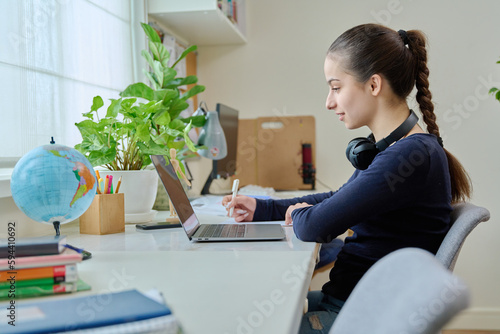 Teen girl studying at home using laptop sitting at desk