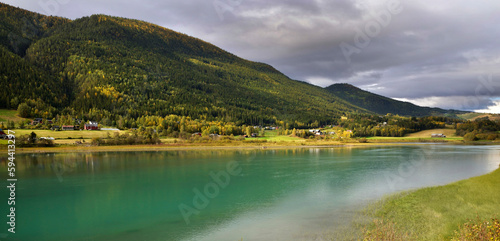 beautiful view on sea water in norway with green hills and village under cloudy sky