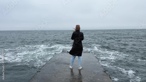 Back view of girl standing alone on pier near the sea in a storm. Woman standing near storm waves hitting the pier. photo