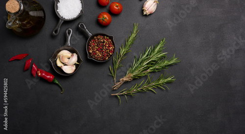 Fototapeta Naklejka Na Ścianę i Meble -  Miniature pans with spices, salt, black pepper and fragrant pepper, a sprig of rosemary on a black table. Spices for cooking