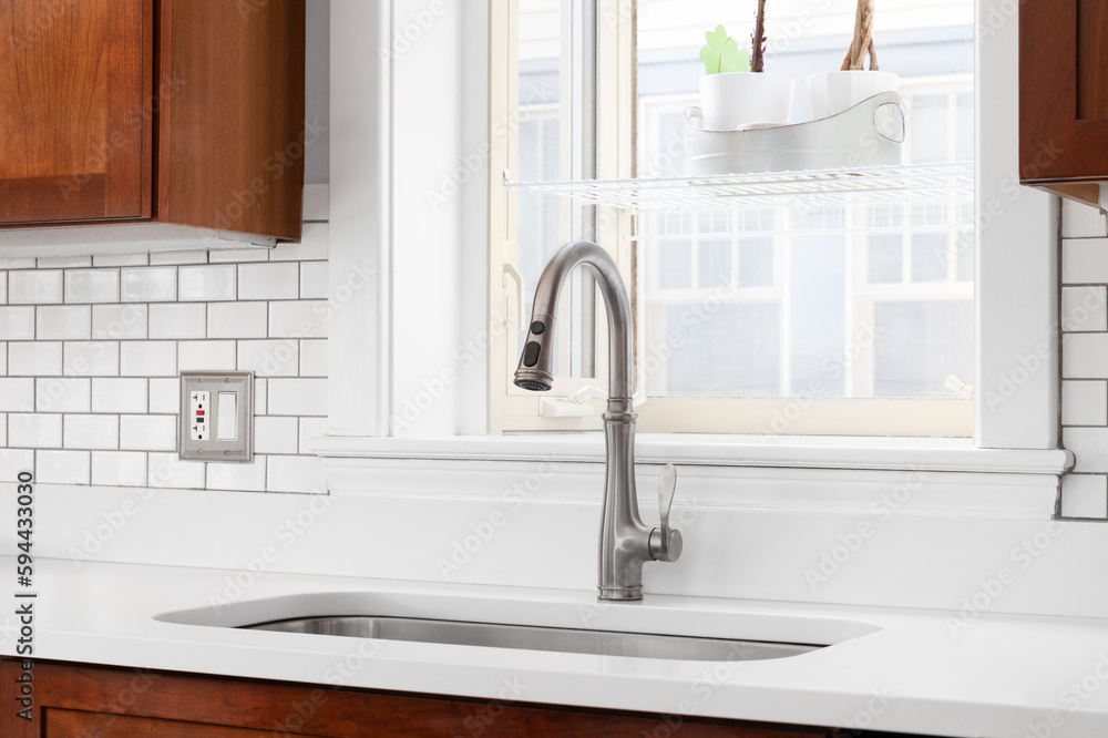 A kitchen sink detail in front of a window with a white marble