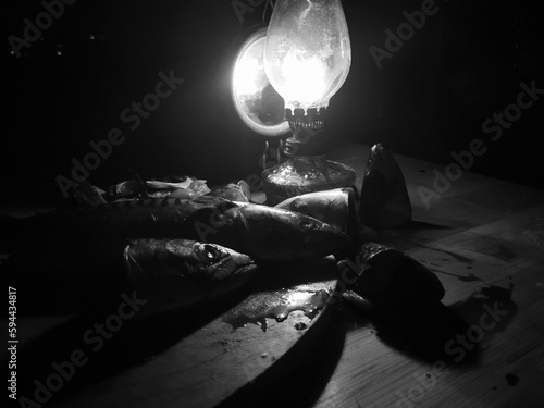 dead fish with kerosene lamp and lamp light illumination. Dead mackerel fish on the wooden board with Kerosene wick lamp photo