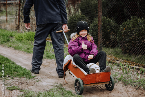 A strong adult man, father, grandfather rides, carries on a rusty old cart, wagon along the road in the village, countryside, a small beautiful smiling, happy girl, child. Photography, portrait.