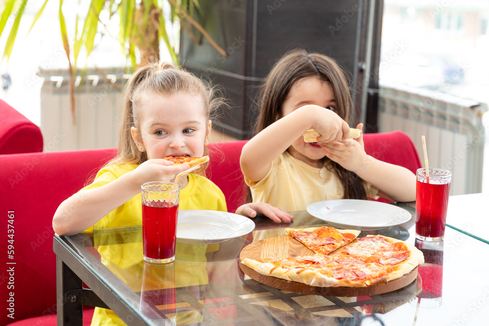 Small cute girls eat pizza. A little adorable girls eat pizza with great pleasure in a restaurant. Spending time with family or in a warm circle of friends. Have fun with the best friends. Small cute girls eat pizza. A little adorable girls eat pizza with great pleasure in a restaurant. Spending time with family or in a warm circle of friends. Have fun with the best friends.