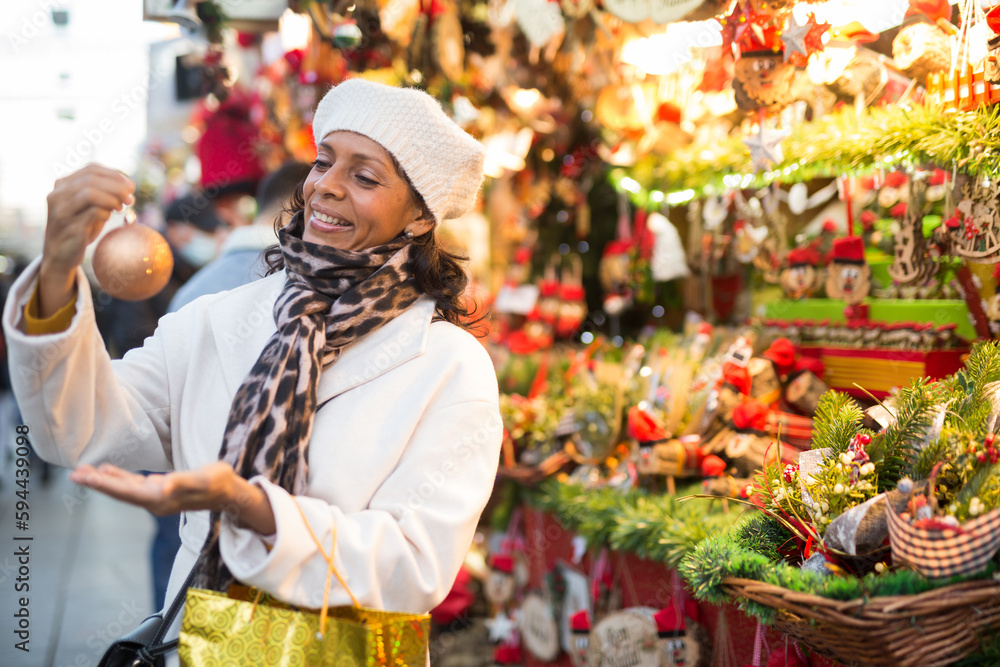 Hispanic woman standing at gift shop while visiting christmas fair and choosing christmas decorations.