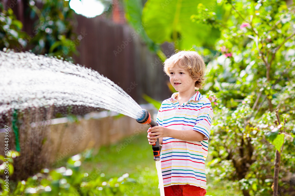 Boy watering flower in garden. Kid with water hose Boy watering flower in garden. Kid with water hose