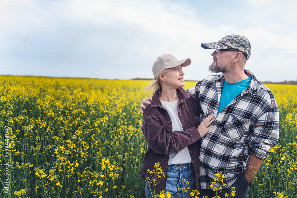 Young adult caucasian couple of farmers standing embracing in a spring blooming rapeseed field