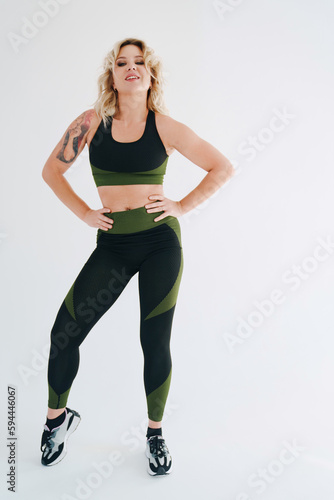 an attractive blonde in a black and green tracksuit poses on a white background.