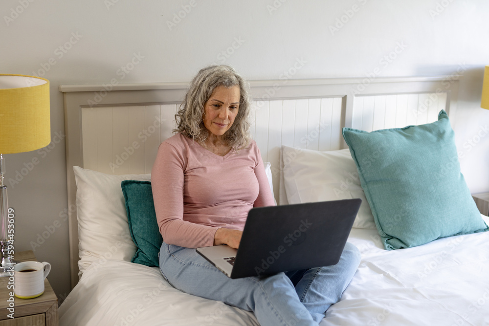 Happy senior caucasian woman sitting on bed and using laptop Happy senior caucasian woman sitting on bed and using laptop