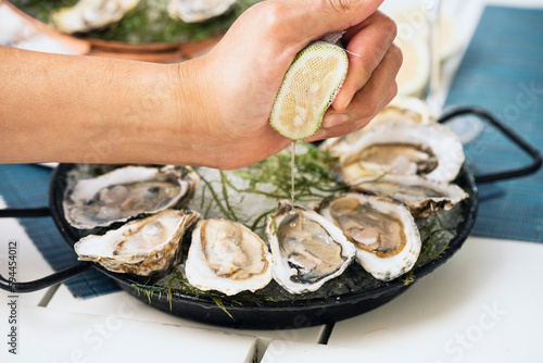 Canvastavla ostras frescas al natural en plato negro con limón exprimido por una mano en fon