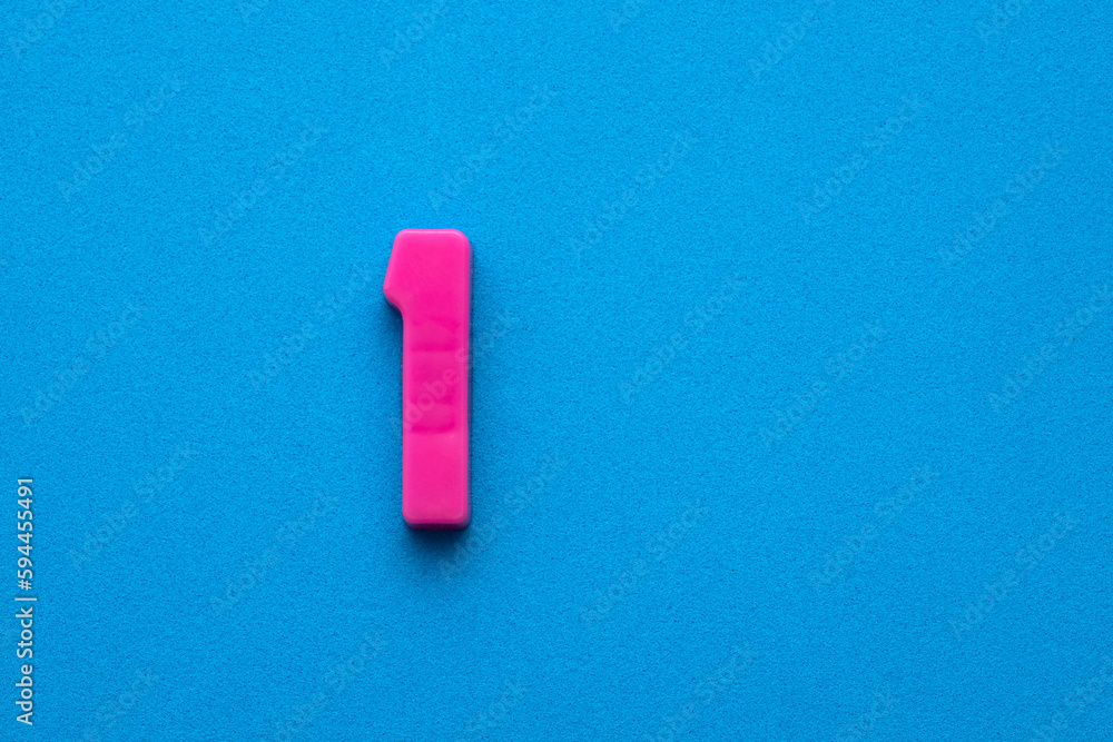 Number one color pink (1) - Plastic digit on blue foamy colored background Number one color pink (1) - Plastic digit on blue foamy colored background