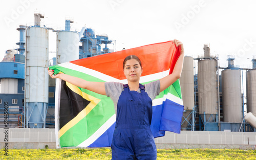 Calm young woman worker posing with South Africa flag in hands against background of factory © JackF