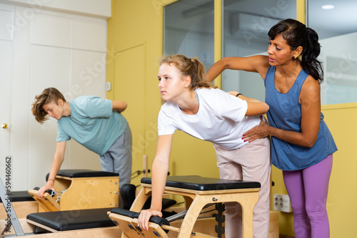 Teenager boy and girl exercising with pilates trainer latin woman in gym. They're training with pilates reformers.