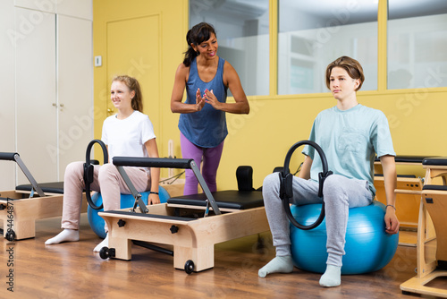 Teenagers under the guidance of pilates trainer are engaged with gymnastic ring on a ball