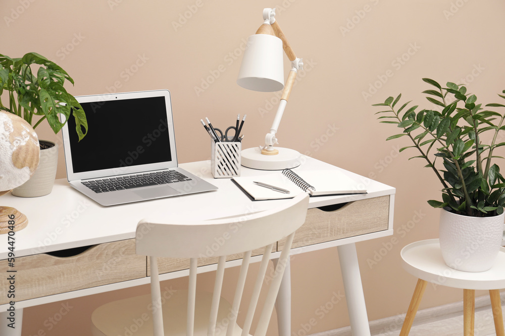 Fototapeta premium Cozy workplace with modern laptop on desk and comfortable chair at home