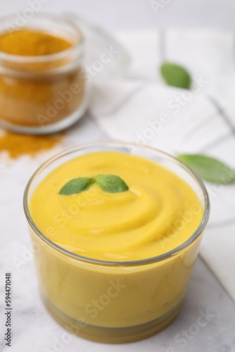Tasty curry sauce, powder and basil leaves on white table, closeup
