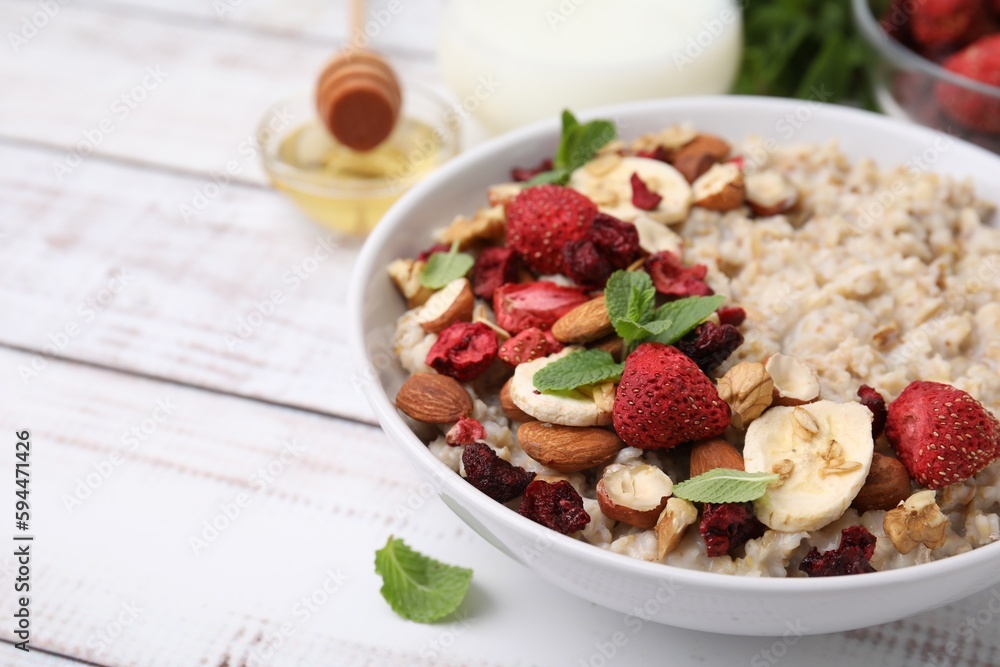 Delicious oatmeal with freeze dried berries, banana, nuts and mint on white wooden table, closeup. Space for text Delicious oatmeal with freeze dried berries, banana, nuts and mint on white wooden table, closeup. Space for text