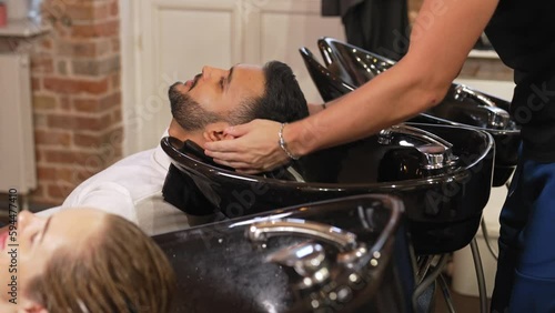 Barber fixing man head in a shampoo bowl and fixing the water temperature before washing hair in a salon. High quality 4k footage photo