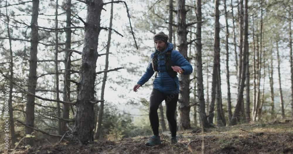 Trail runner in the woods running on a forest path and jumping. Man wearing winter sports outfit. Sun shining between trees. Recorded at 120 fps. Trail runner in the woods running on a forest path and jumping. Man wearing winter sports outfit. Sun shining between trees. Recorded at 120 fps.
