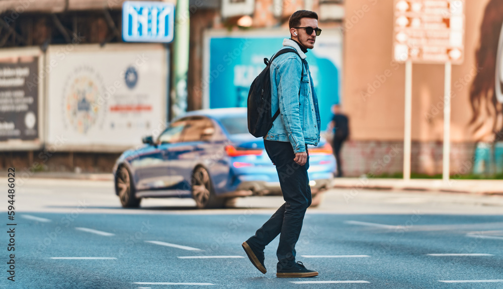 Student walks through the city wearing sunglasses, carrying a backpack, and using wireless headphones, embodying the modern urban lifestyle and the ability to stay connected while on-the-go.