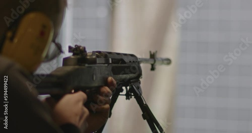 Shooter aiming and firing a Ruger Mini-14 rifle at a shooting range in slow motion. A spent casing gets ejected from the weapon photo