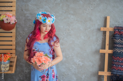 Beautiful red haired asian girl wearing blue flowers holding soft red flowers with soft light while looking to the copy space.