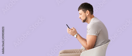 Man with bad posture using mobile phone while sitting on chair against lilac background