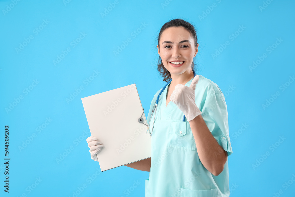 Female medical assistant with folder showing thumb-up on light blue background Female medical assistant with folder showing thumb-up on light blue background